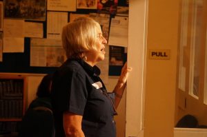 A side photo of a woman standing away from the hollow square, looking towards them (out of shot) and singing.