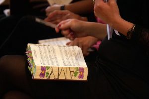 A close up, cropped photograph of an open Sacred Harp Denson book sitting open on a woman’s lap. The end pages of the book have been decorated with the name “Amy” in capital letters with flowers either side. 