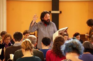 A man with a beard leads a song from the hollow square while holding his song book. 