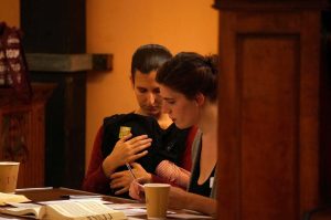 A candid photo from far away showing two women at the arranging table, where the order of singers is decided. They are looking at papers on the table. 