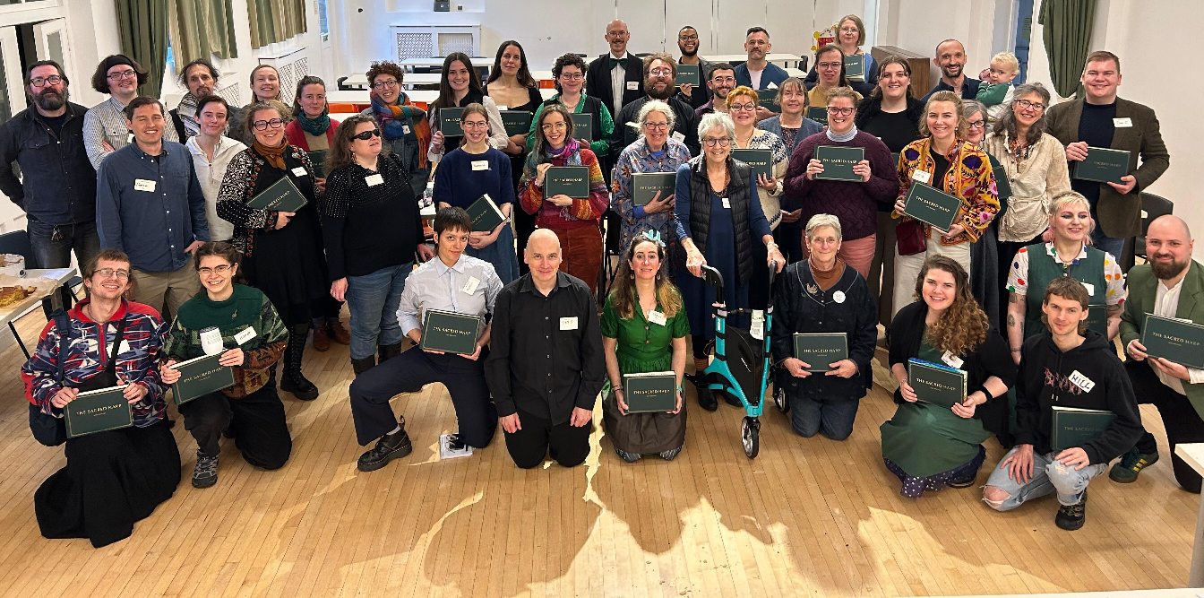 A large group of approximately 40 people of all ages, assembled together in a hall and posing or smiling for the photograph. The occasion is the London All Day singing 2025, where singers used the new 2025 edition or "Green Book" for the first time at a London all day singing. Most of them are wearing green clothing and holding songbooks. A large group of approximately 40 people of all ages, assembled together in a hall and posing or smiling for the photograph. The occasion is the London All Day singing 2025, where singers used the new 2025 edition or "Green Book" for the first time at a London all day singing. Most of them are wearing green clothing and holding songbooks.